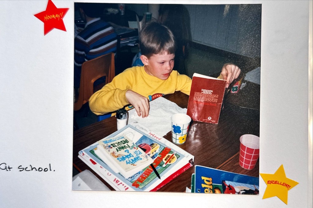 author Joseph in elementary school.  he is eating popcorn and reading "The Chocolate Touch" by Patrick Skene Catling,