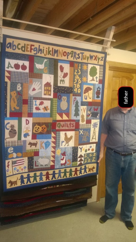 a photo of Father standing next to an impressive homemade quilt on a homemade quilt rack